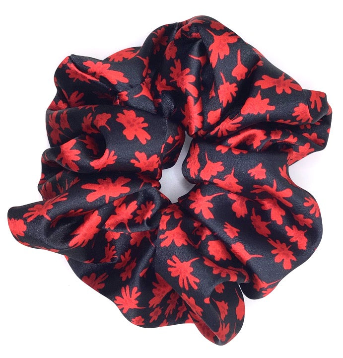 An XXL satin scrunchie with a red flower design on a black background lying on a white surface.
