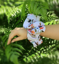 Load image into Gallery viewer, A white XXL charmeuse scrunchie with a watercolor floral design is wrapped around a wrist.
