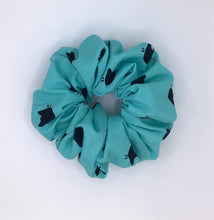 Load image into Gallery viewer, Cotton scrunchie made from blue-teal fabric with cute and simple cat face designs, perfect for adding a fun and playful touch to any hairstyle.

