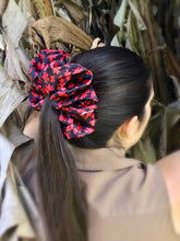 Load image into Gallery viewer, A long haired brunette woman&#39;s hair tied up in a high ponytail with an XXL satin scrunchie featuring a red flower design on a black background.
