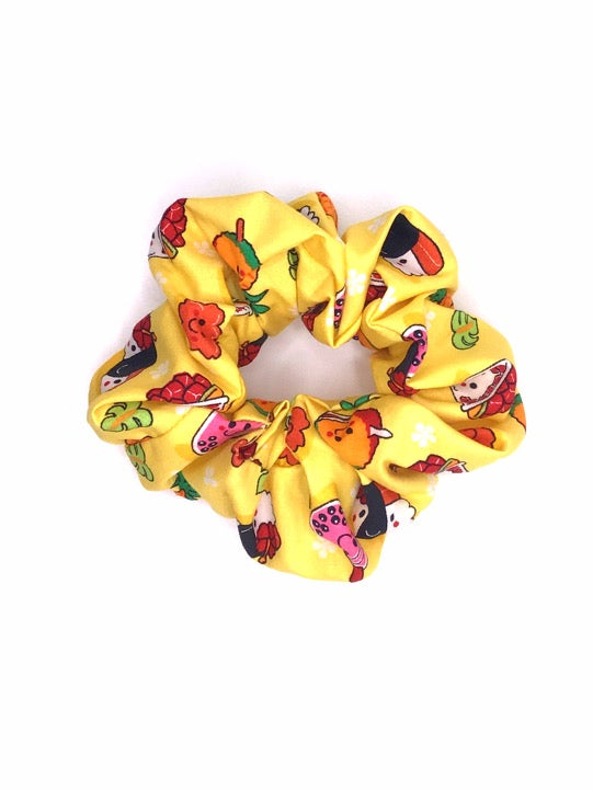 A cotton scrunchie featuring Hawaiian local childhood favorites such as pineapple, poke bowl, spam musubi, milk tea, and shave ice on a yellow background.