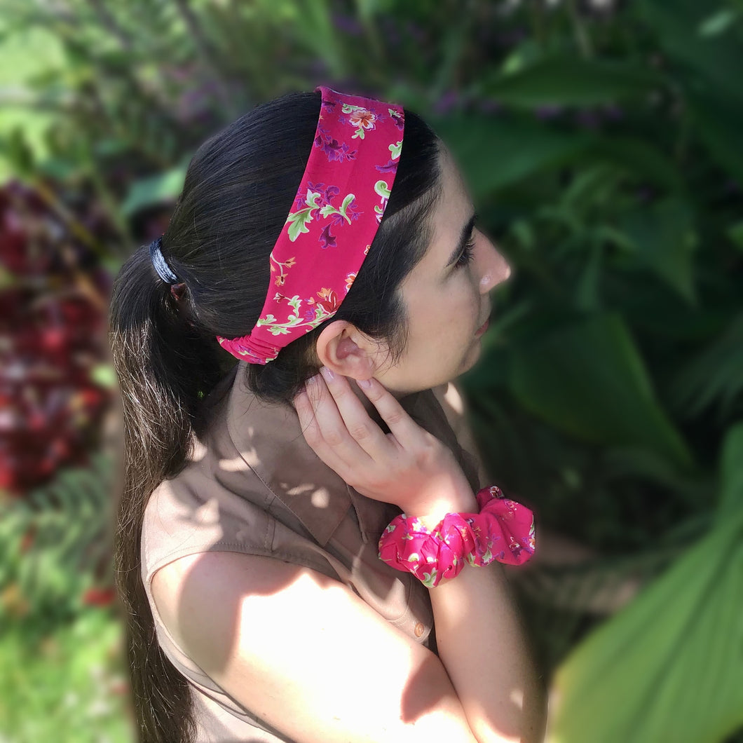 A dark-haired woman wearing a pink flat cotton headband with a lovely floral pattern featuring green leaves and pink and purple flowers on a pretty pink background, adding a touch of colorful charm to her outfit.