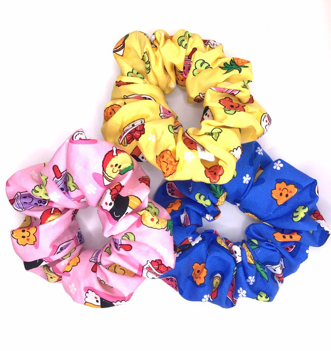Three cotton scrunchies featuring Hawaiian local childhood favorites such as pineapple, poke bowl, spam musubi, milk tea, and shave ice on a yellow, blue, or pink background.