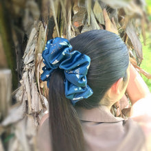 Load image into Gallery viewer, A long haired brunette woman wearing a grey-blue XXL satin scrunchie with a floral and dragon design, holding her hair in a ponytail.
