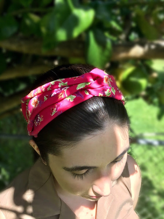 A dark-haired woman wearing a pink knotted cotton headband with a lovely floral pattern featuring green leaves and pink and purple flowers on a pretty pink background, adding a touch of colorful charm to her outfit.